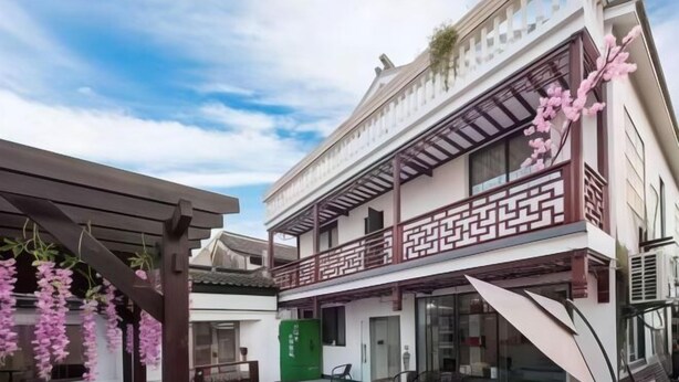 Un bâtiment de style traditionnel, à deux étages, doté d’un balcon avec une balustrade ornée et d’un espace extérieur aménagé avec des chaises et des tables.