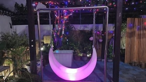 Un hamac suspendu, illuminé par une lumière douce, entouré de plantes et délimité par une clôture en bambou.