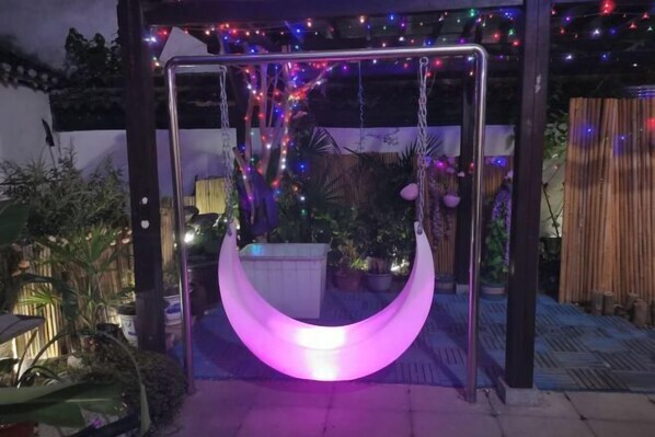 A hammock swing with a glowing light, surrounded by plants and a bamboo fence. - Jingdaihuakai Inn (Suzhou)