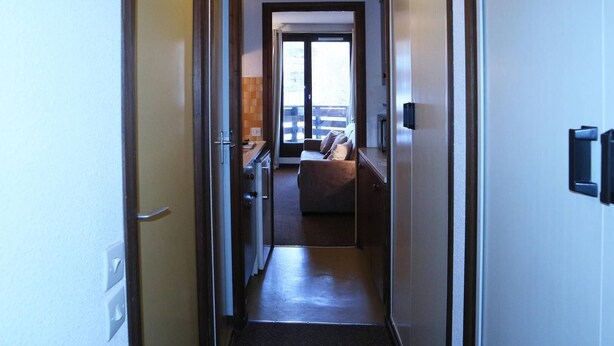 A narrow hallway leading to a bedroom with a bed and a window.