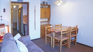 A cozy living room with a wooden dining table and chairs, a sofa, and a kitchen area visible through an open door.