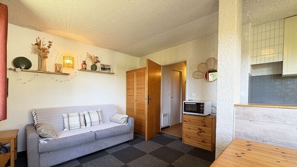 A compact living space with a sofa, a wooden dining table, a microwave, and a small kitchen area. - 12 LA Seille Studio 4 Personnes (LES ORRES 1650)