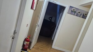 Un corridoio con pavimento in legno, un estintore e una porta che dà su una stanza.