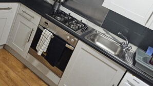 Una cucina con mobili bianchi, una cappa in acciaio inossidabile, un piano cottura a gas, forno integrato, lavastoviglie e un piano di lavoro nero.