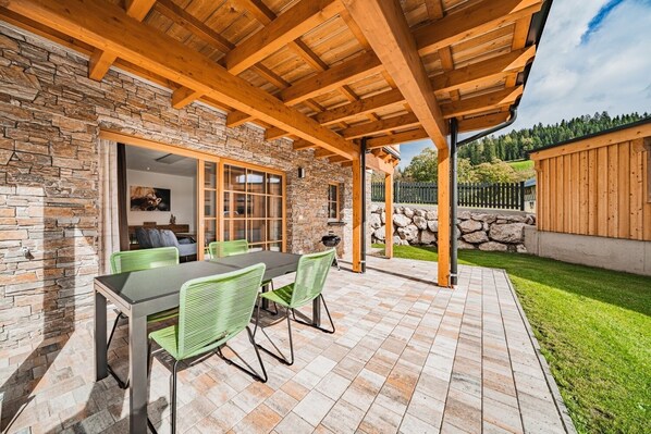 Une terrasse couverte avec un mur en pierre, des poutres en bois et un sol carrelé.