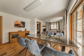 Un espace repas moderne avec une table en verre, des chaises à revêtement gris, des meubles en bois et une grande fenêtre agrémentée de rideaux.