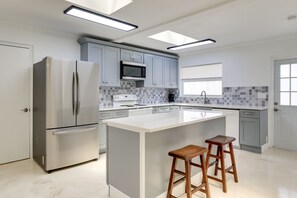A modern kitchen with a stainless steel refrigerator, a microwave, and a large island with two wooden stools. - Dog-Friendly Home w/ Patio & BBQ in Bradenton (Bradenton)