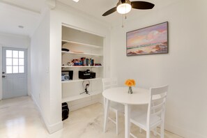 A room with a white ceiling fan, a white table with two chairs, a bookshelf with various items, and a painting of a beach scene. - Dog-Friendly Home w/ Patio & BBQ in Bradenton (Bradenton)