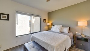 Une chambre à coucher avec un grand lit, un banc, une table de chevet et une fenêtre avec des stores.