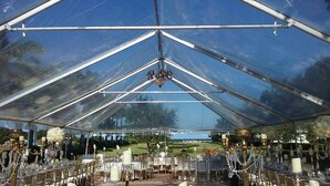 Une grande tente spacieuse et bien éclairée, avec des tables dressées pour un événement, agrémentée d’un lustre et de décorations florales.