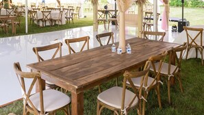 Un espace extérieur aménagé pour les événements, avec une table et des chaises en bois, entouré de tentes blanches et illuminé de guirlandes lumineuses.
