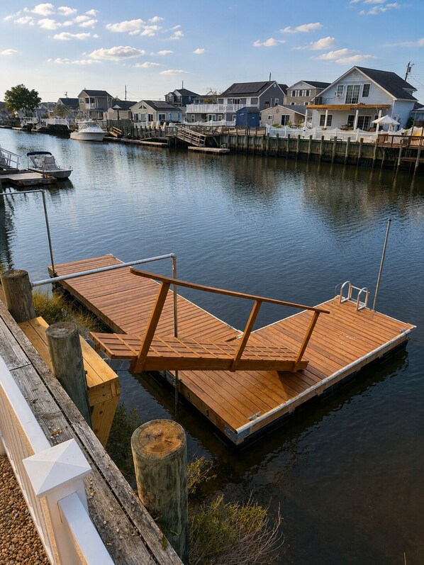 A wooden dock extending into calm water with a row of houses in the background. - Lagoon Home with Dock + Bar -Near Calm, Kid-Friendly Beach (Little Egg Harbor Township)