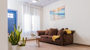 Una sala de estar con un sofá marrón, una mesa de centro blanca y dos plantas en macetas.