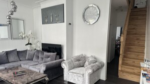 A modern living room with a grey sofa, a patterned armchair, a marble coffee table, and a decorative clock on the wall. - House - Sleeps 6 - Garden - Seaside - Pet Friendly (Great Yarmouth)