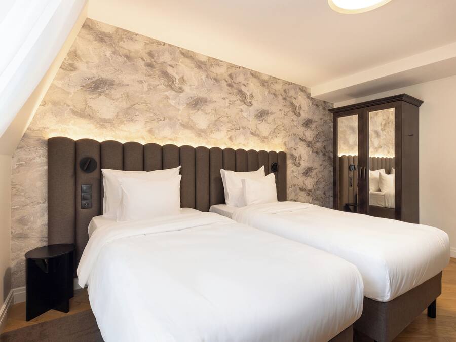 Ein modernes Hotelzimmer mit zwei Betten, einer Wand mit Marmoroptik, einem dunklen Kopfteil und einem großen Spiegelkorpus.