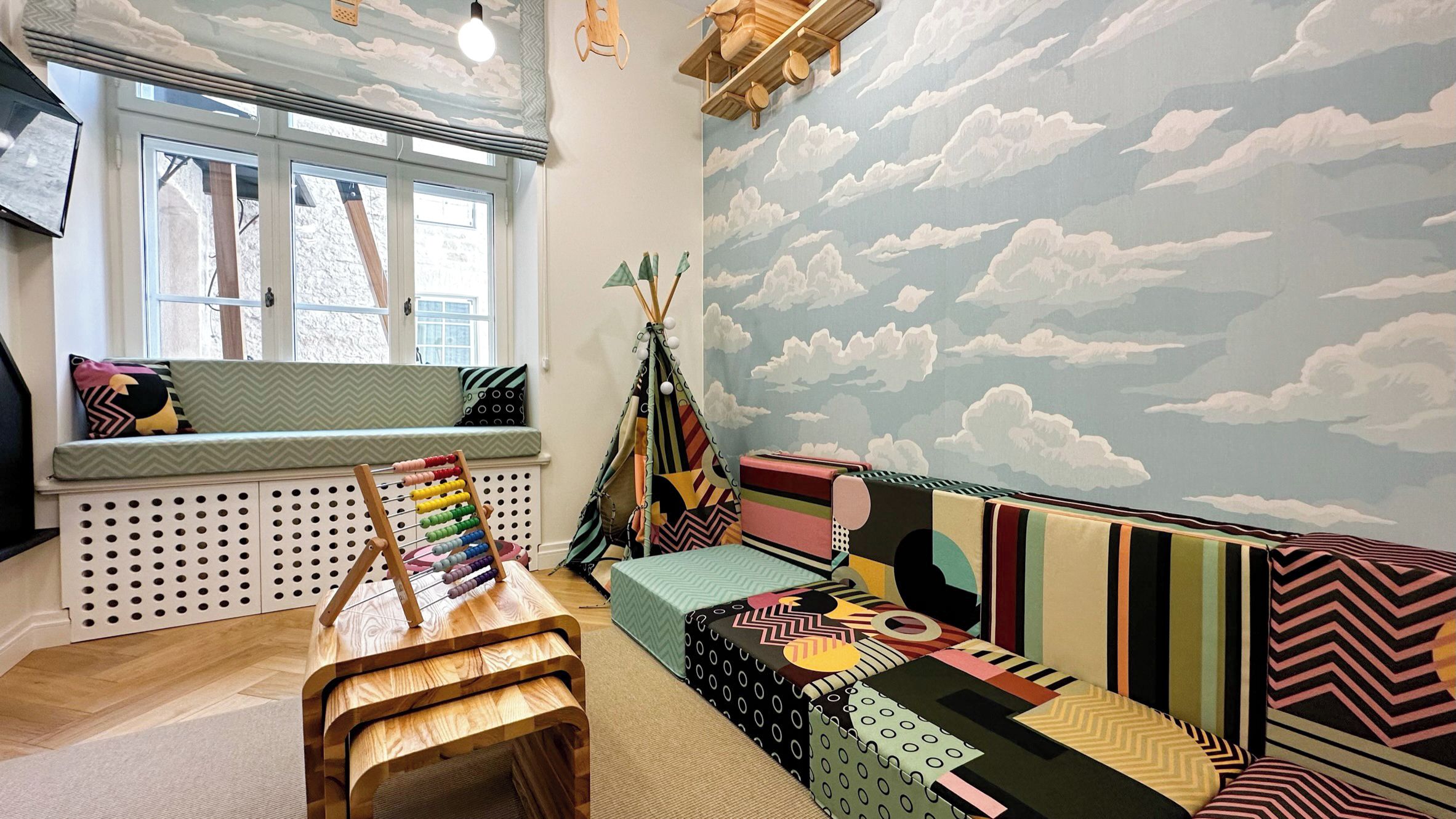A cozy room with a window, a wooden play table, a colorful bean bag area, and a wall mural.
