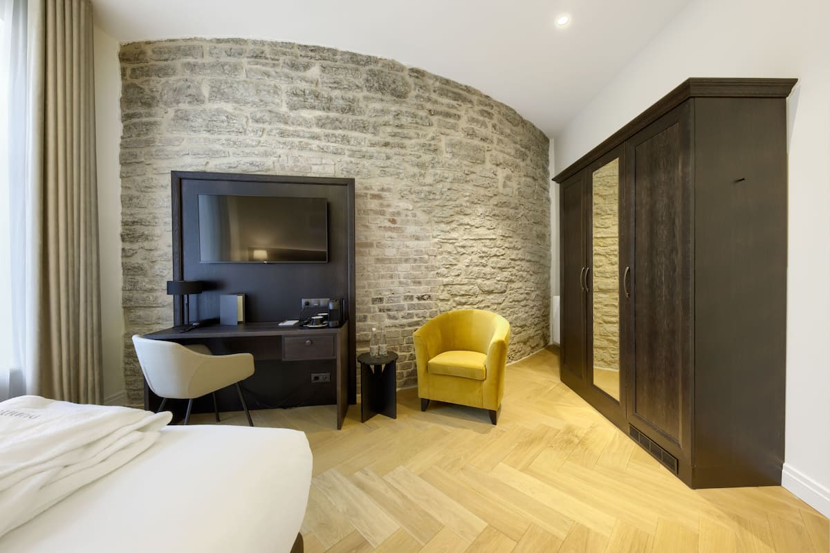 Ein Hotelzimmer mit Steinwand, einem Bett, einem Schreibtisch mit Stuhl, einem Fernseher und einem Kleiderschrank.