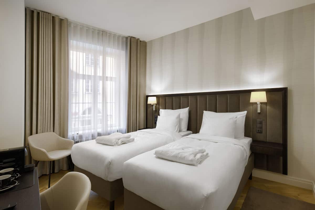 Ein Hotelzimmer mit zwei Betten, einem Schreibtisch, einem Stuhl und einem Fenster mit Vorhängen.
