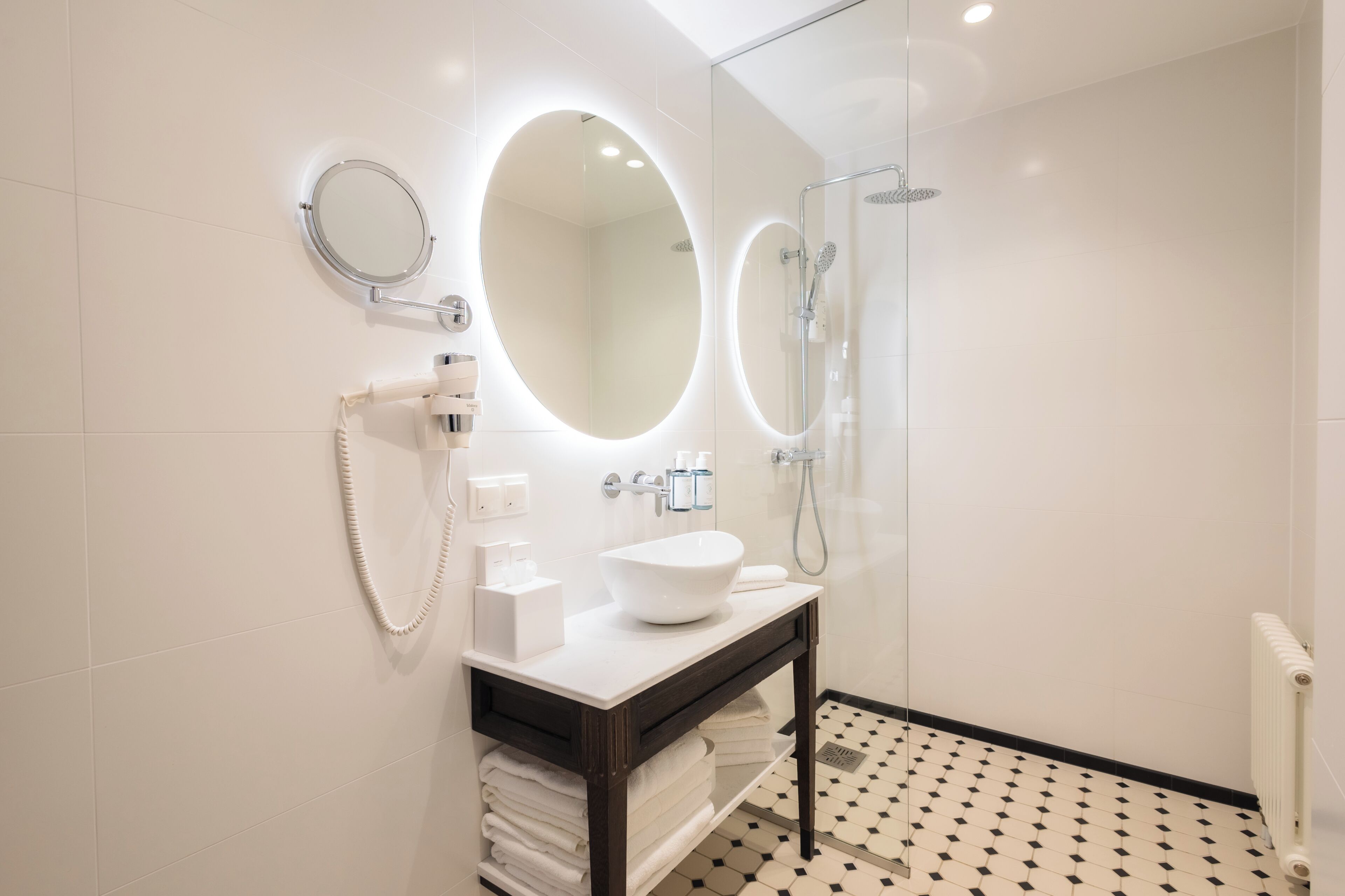 Un baño moderno con un lavamanos blanco, un espejo grande y una ducha con mampara de vidrio.