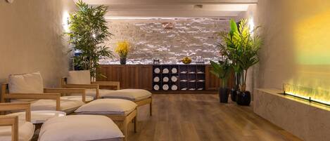 A spa room with wooden floors, multiple seating areas, and a stone wall backdrop.