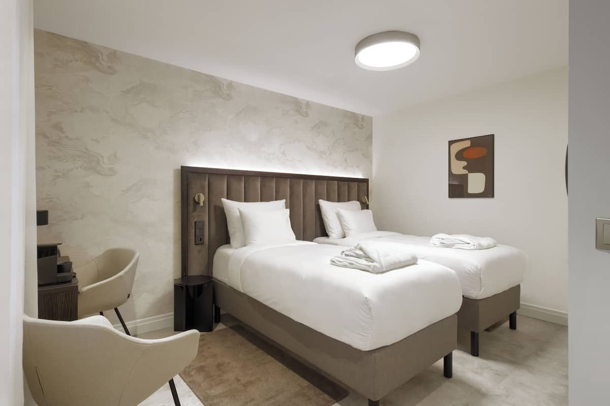 Ein modernes Hotelzimmer mit einem großen Bett, zwei Nachttischen, einem Sessel und einem kleinen Schreibtisch.