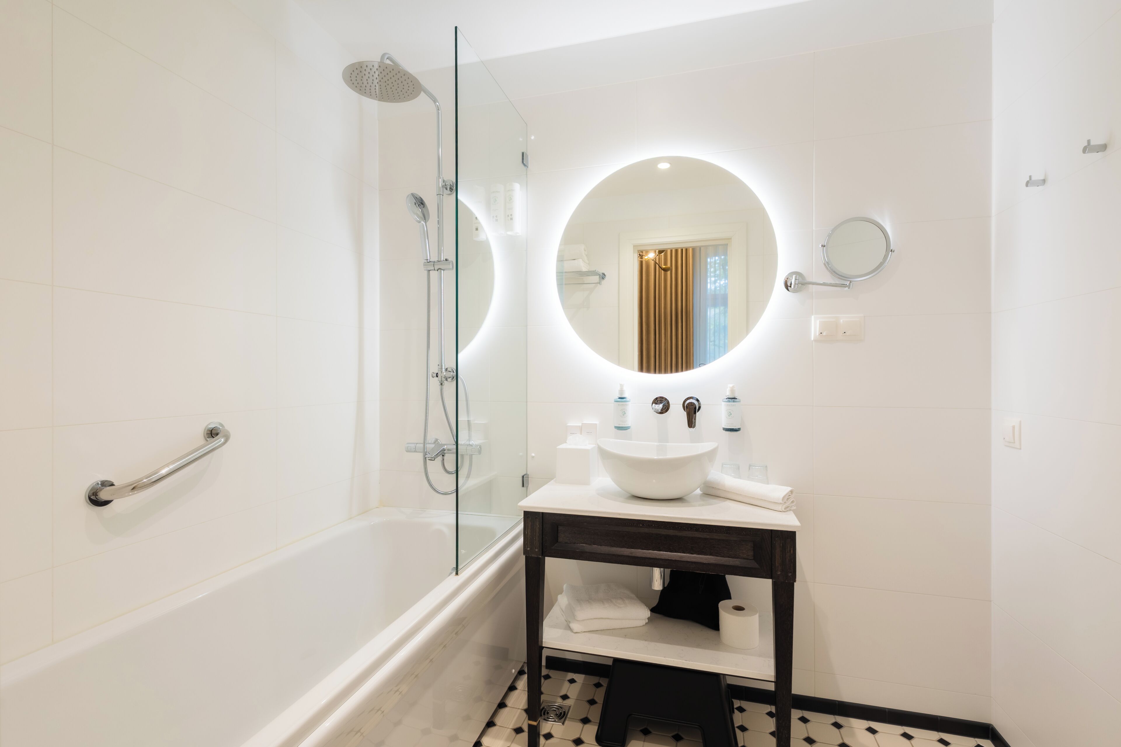 A modern bathroom with a glass-enclosed shower, a round mirror, and a white sink with a dark countertop.