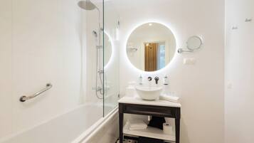 A modern bathroom with a glass-enclosed shower, a round mirror, and a white sink with a dark countertop.