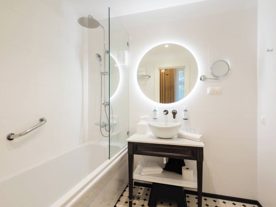 A modern bathroom with a glass-enclosed shower, a round mirror, and a white sink with a dark countertop.