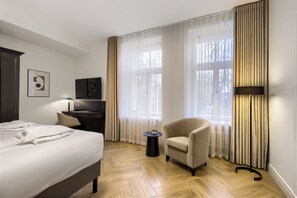 Een hotelkamer met een bed, een stoel, een bureau, een lamp en grote ramen met gordijnen.
