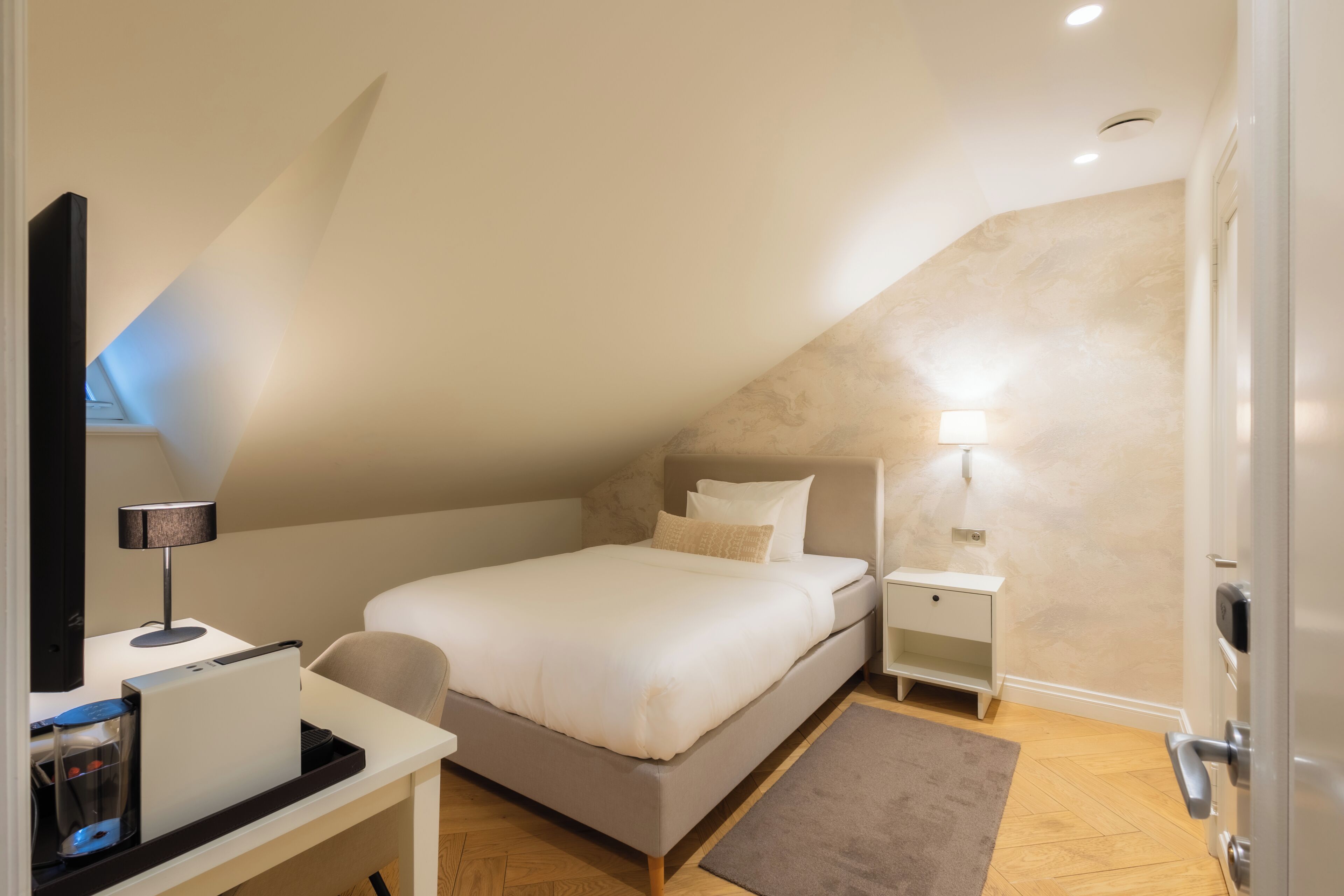 Un dormitorio con cama, mesitas de noche, un escritorio con lámpara y una puerta.