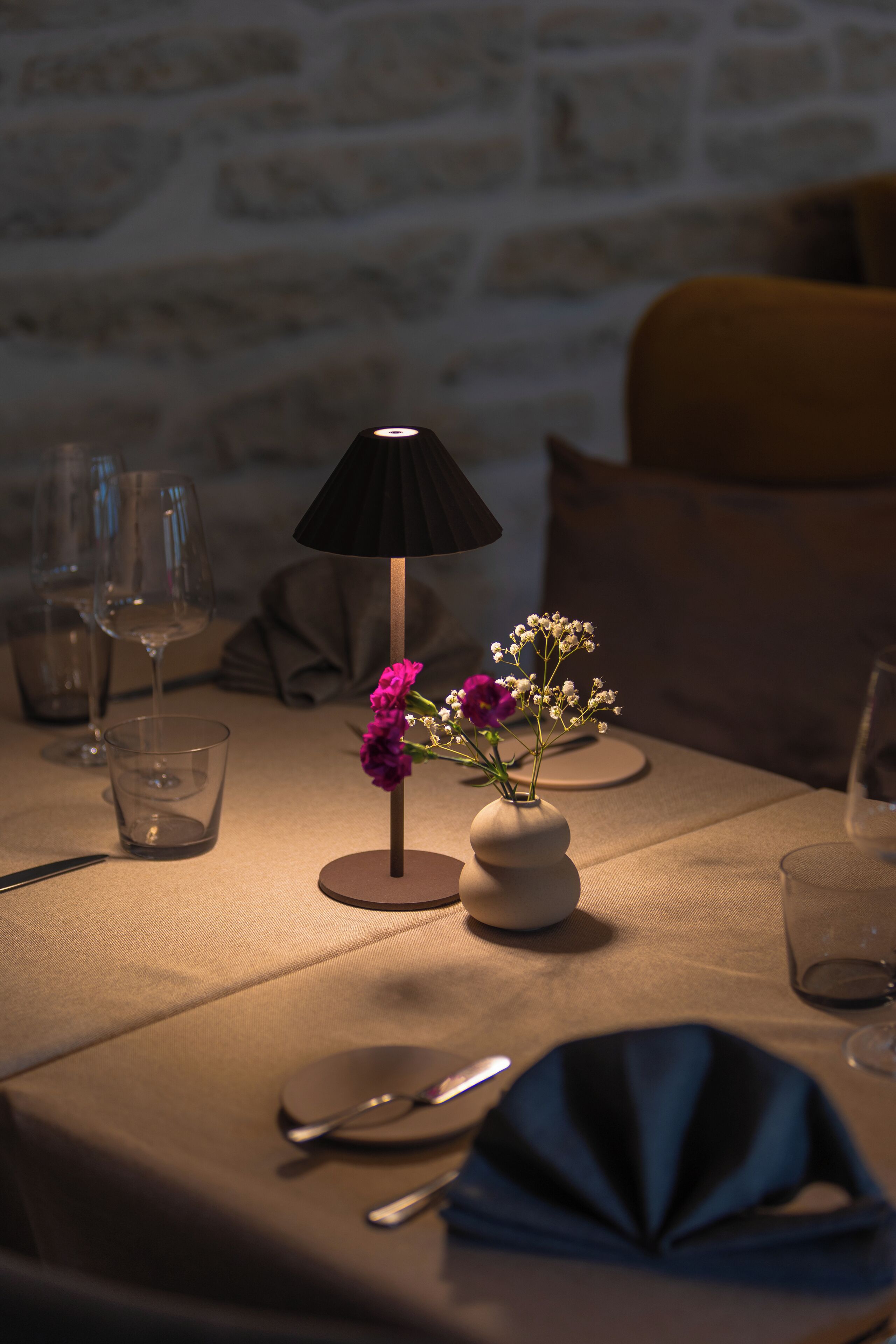Een eettafel gedekt met een bloevas, een lamp en wijnglazen.
