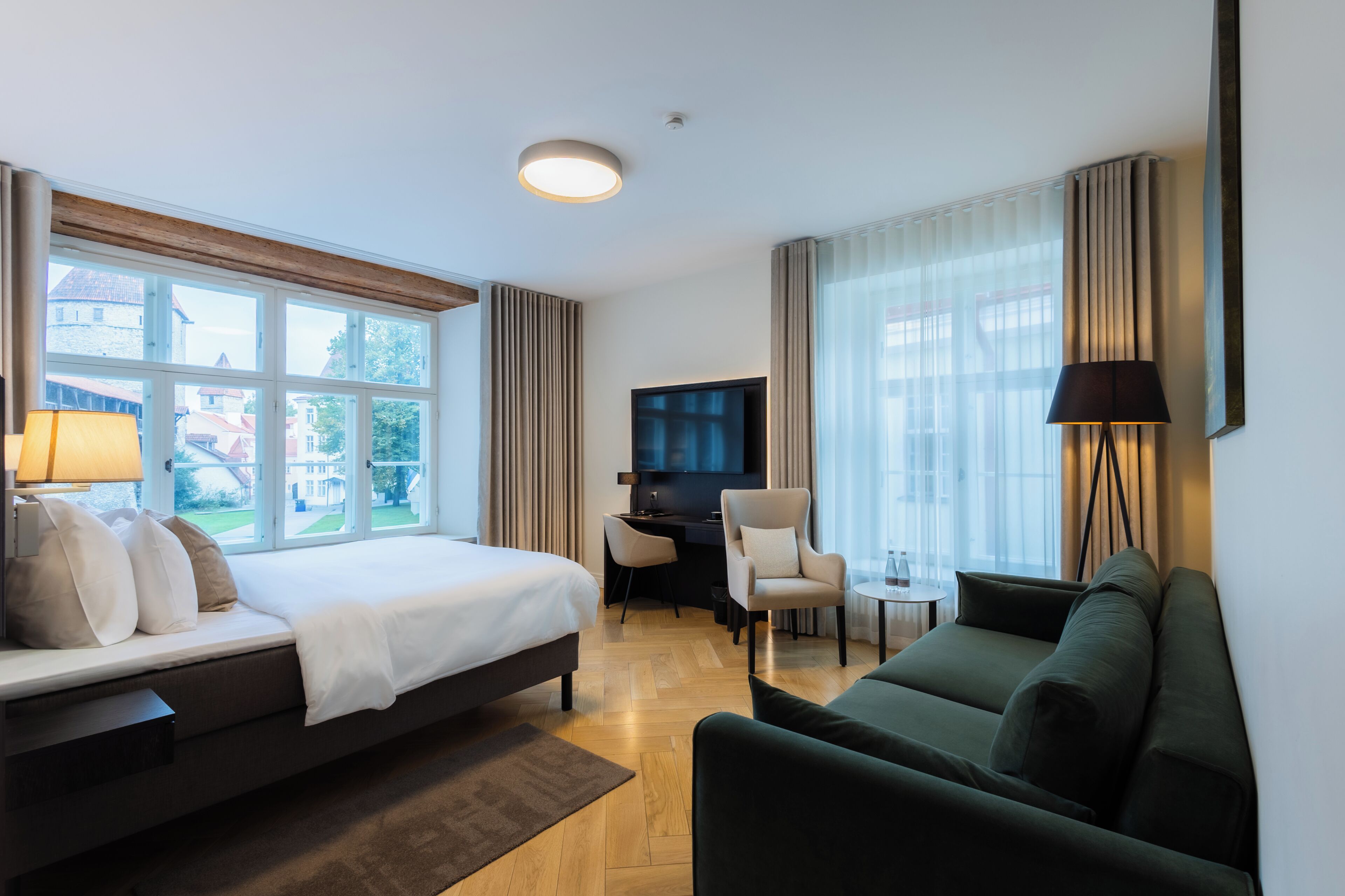 A hotel room with a bed, a desk, a chair, a sofa, and a TV.