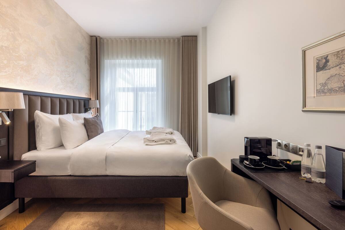 Ein Hotelzimmer mit Bett, Schreibtisch, Stuhl, Fernseher und einem fenster mit Vorhängen.