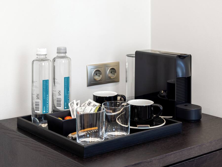 A hotel room's minibar setup with a coffee maker, two bottles of water, and several glasses and mugs.
