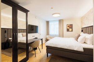 Habitación de hotel con una cama grande, un escritorio, una silla, un televisor y un espejo.