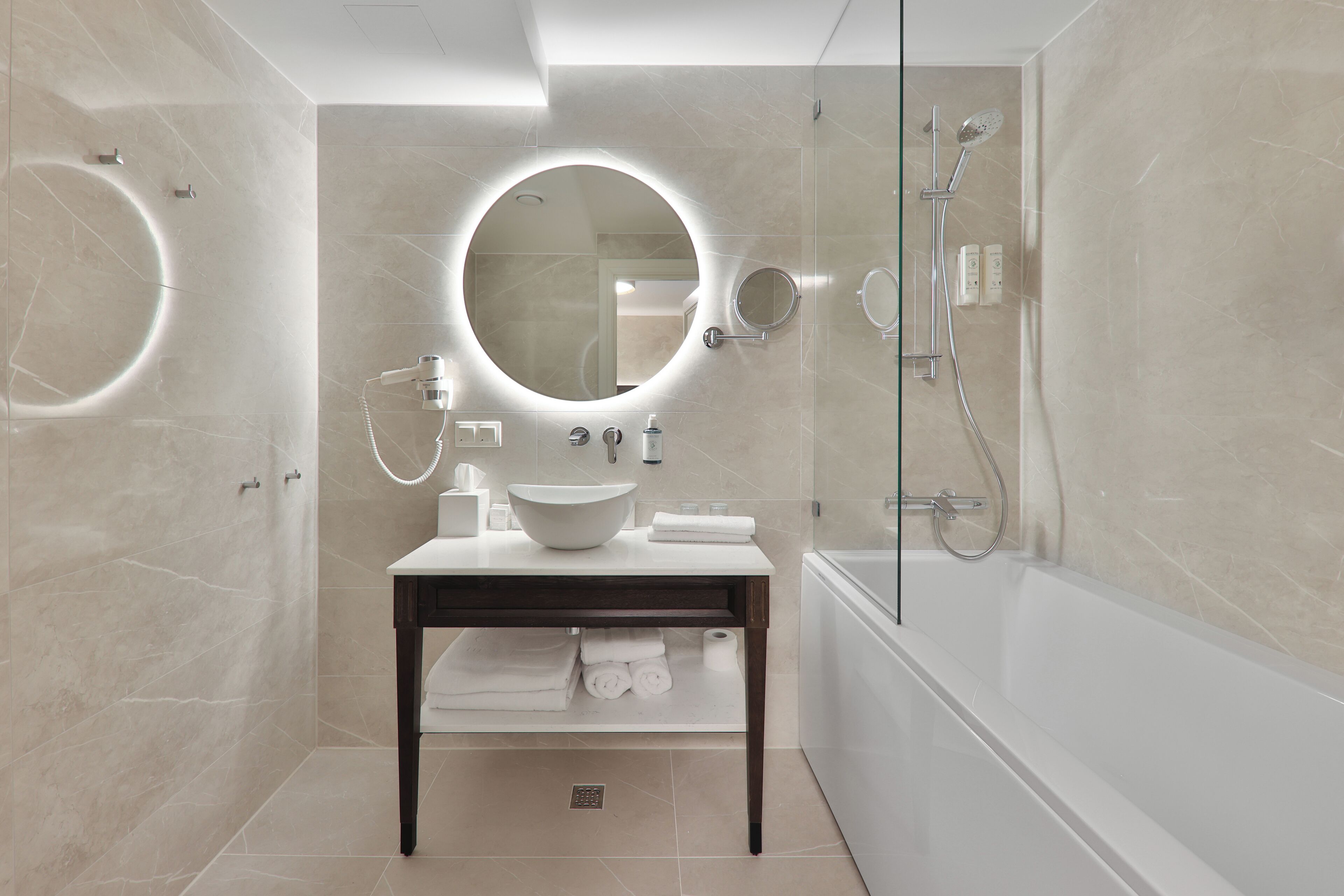 Un baño moderno con un espejo redondo, un lavabo, una bañera y una ducha.