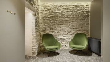 Una habitación con pared de piedra, dos sillas verdes y un radiador.