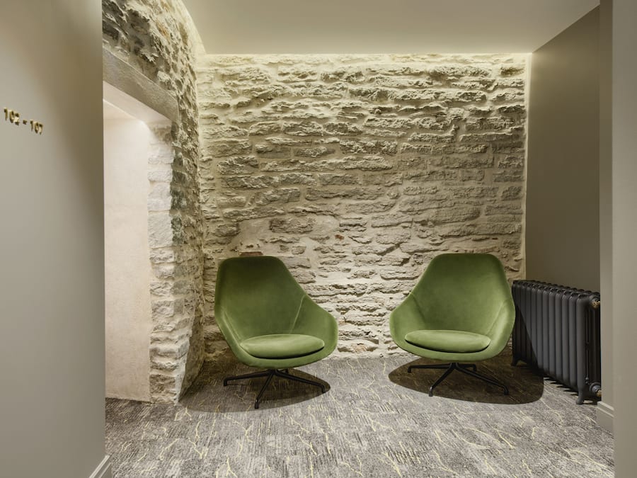 Una habitación con pared de piedra, dos sillas verdes y un radiador.