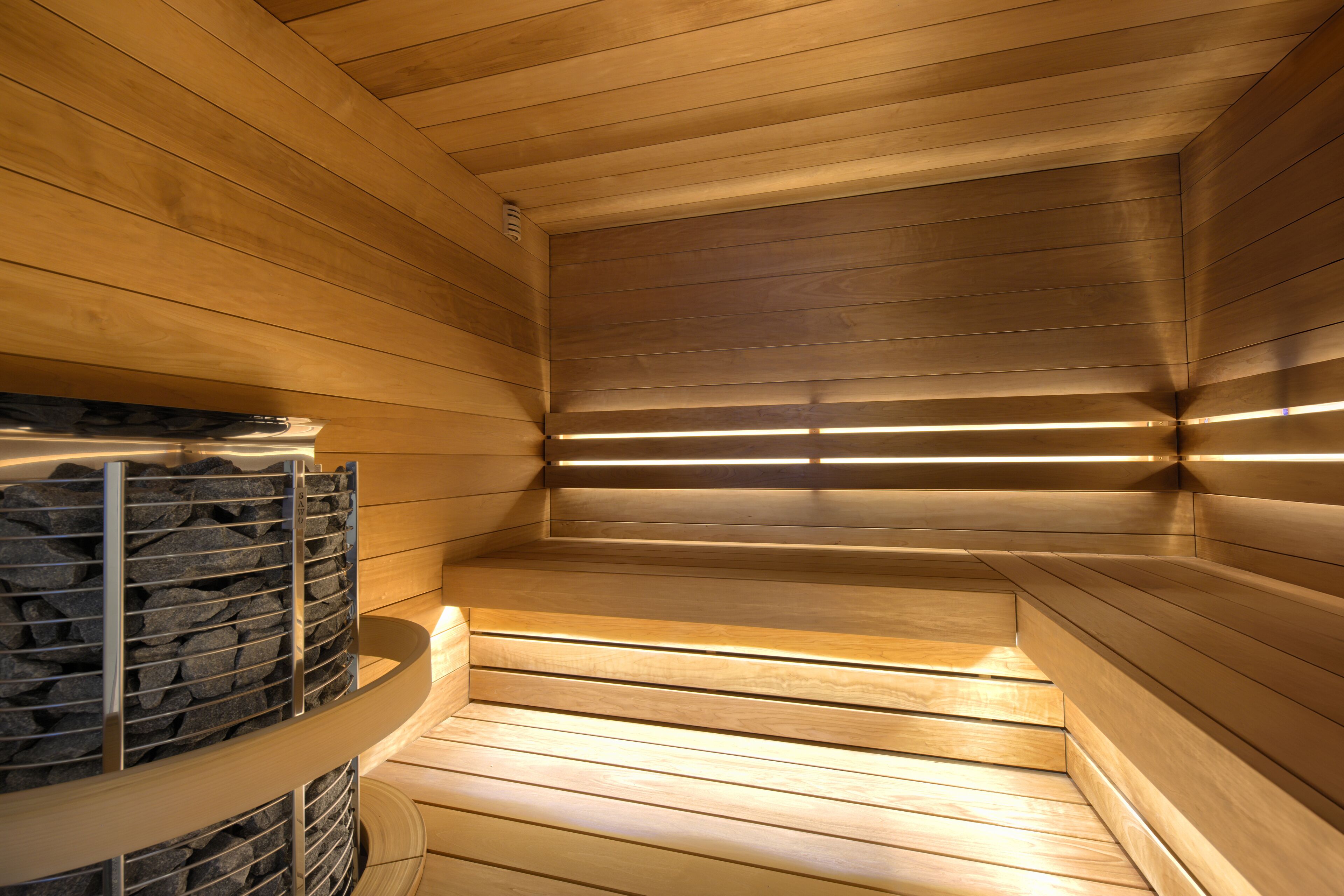 A sauna with wooden walls and benches, a stone wall on the left, and a sloped ceiling.