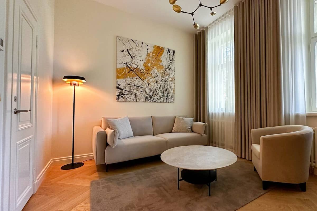Ein modernes Wohnzimmer mit einer Couch, einem runden Couchtisch, einem Sessel, einer Stehlampe und einem großen abstrakten Gemälde.