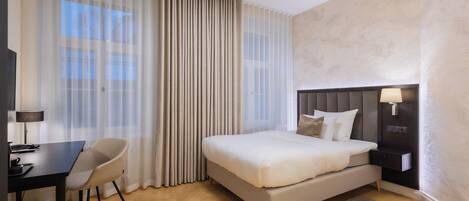 A hotel room with a bed, a desk, a chair, and a nightstand.