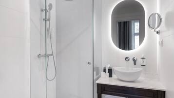 A modern bathroom with a glass shower enclosure, a white sink with a round mirror, and a dark wooden vanity.