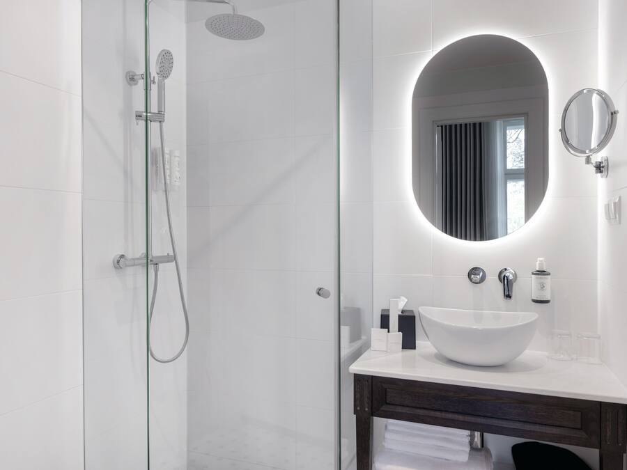 A modern bathroom with a glass shower enclosure, a white sink with a round mirror, and a dark wooden vanity.