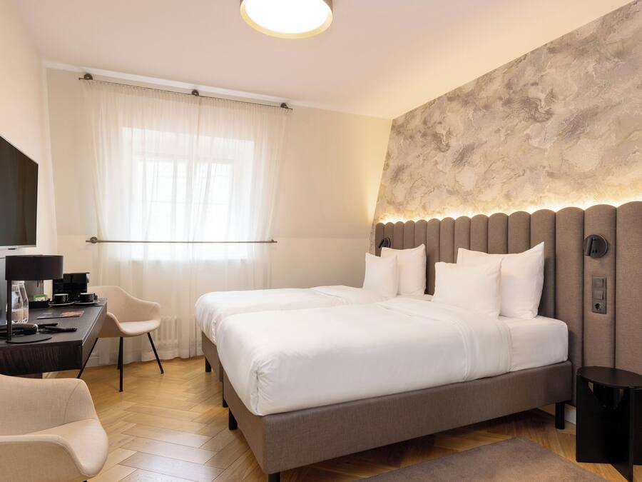 A modern hotel room with a large bed, a desk with a computer, a chair, and a TV.