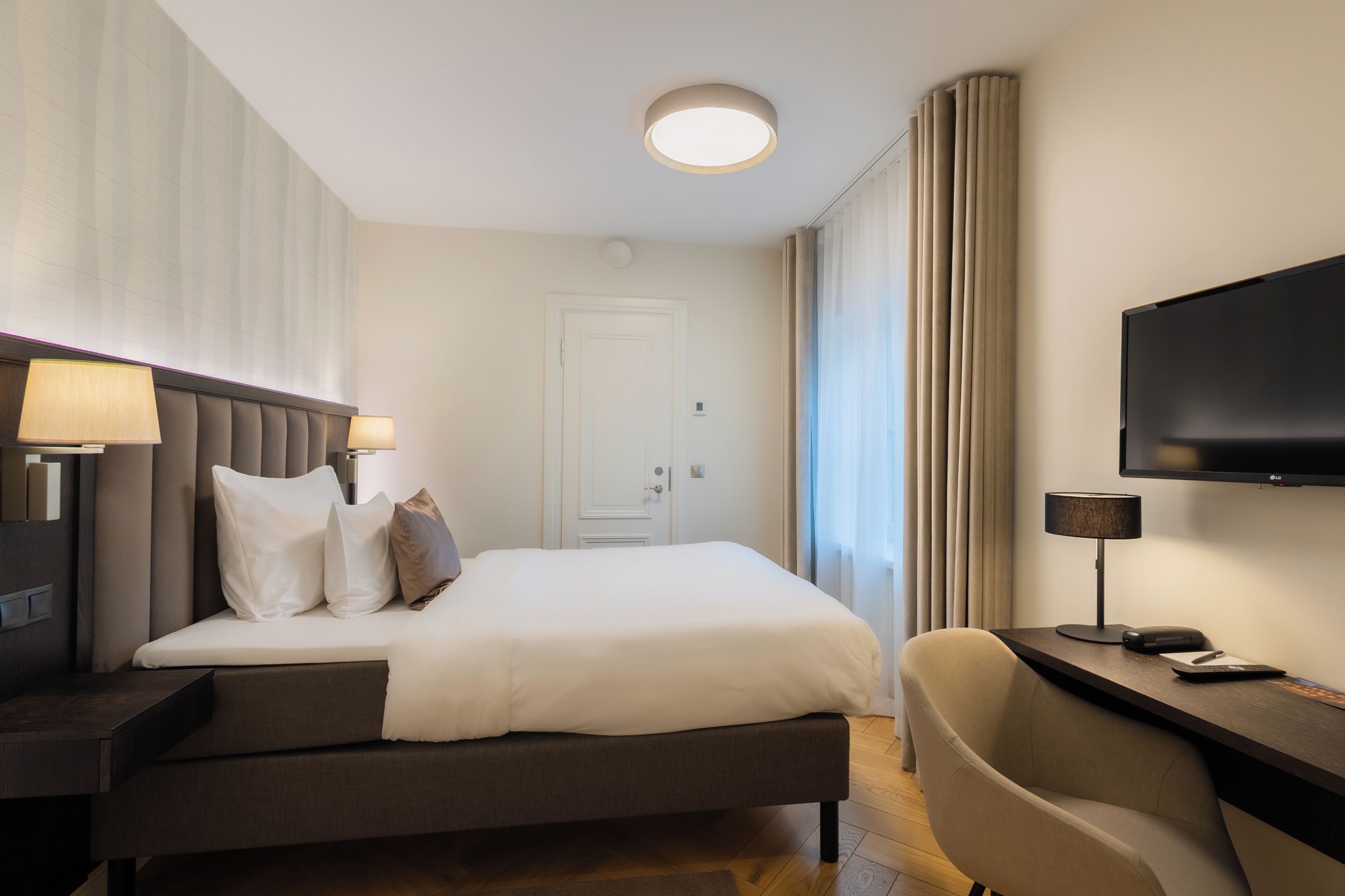 Una habitación de hotel con una cama, lámparas de noche, un escritorio con una silla, un televisor de pantalla plana y una puerta.