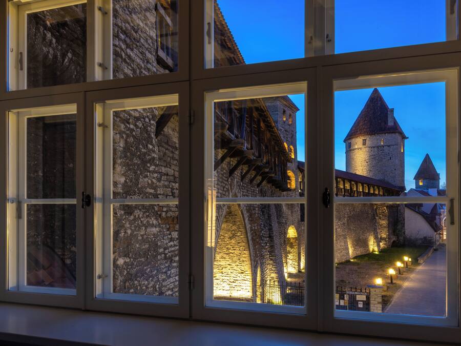 A view through a window of a stone building with a tower, illuminated by interior lighting.