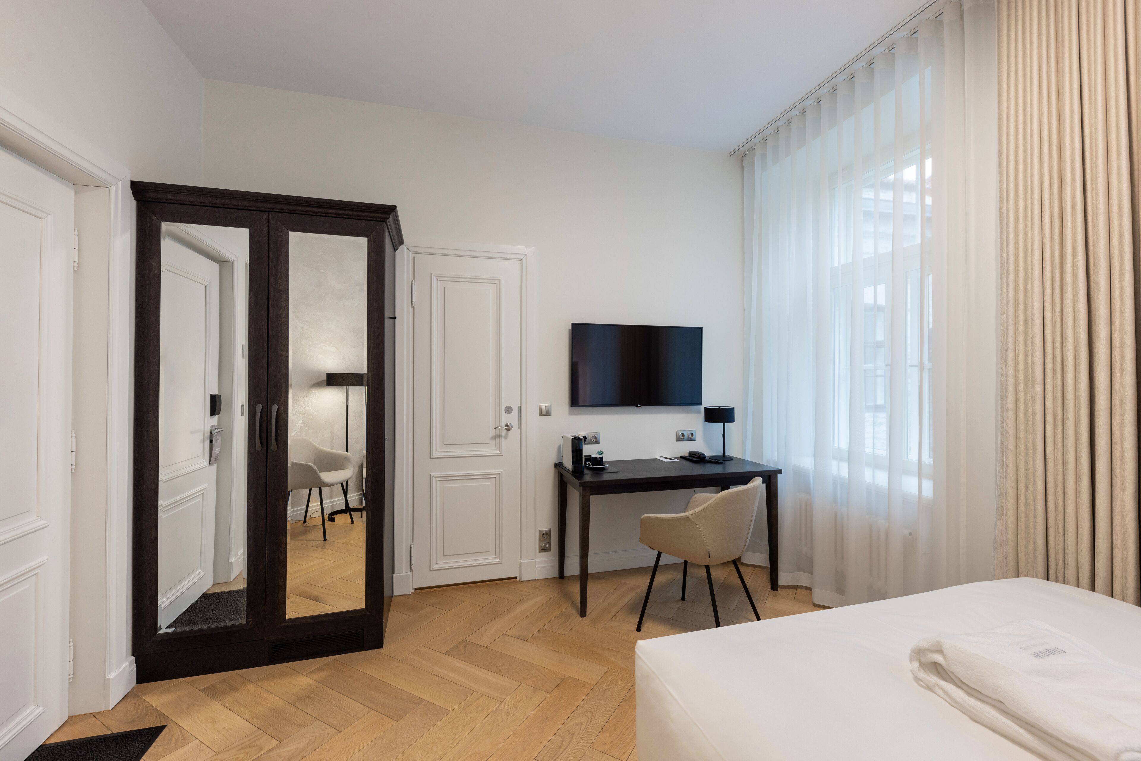 Ein Hotelzimmer mit Bett, Schreibtisch, Stuhl, Fernseher und einem großen Spiegel.