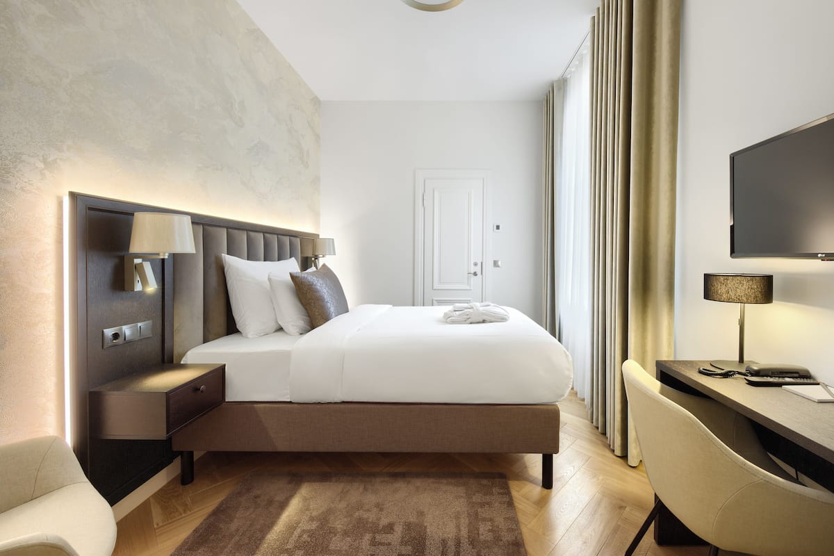 Ein modernes Hotelzimmer mit einem großen Bett, Nachttischen, einem Schreibtisch und einem Flachbildfernseher.