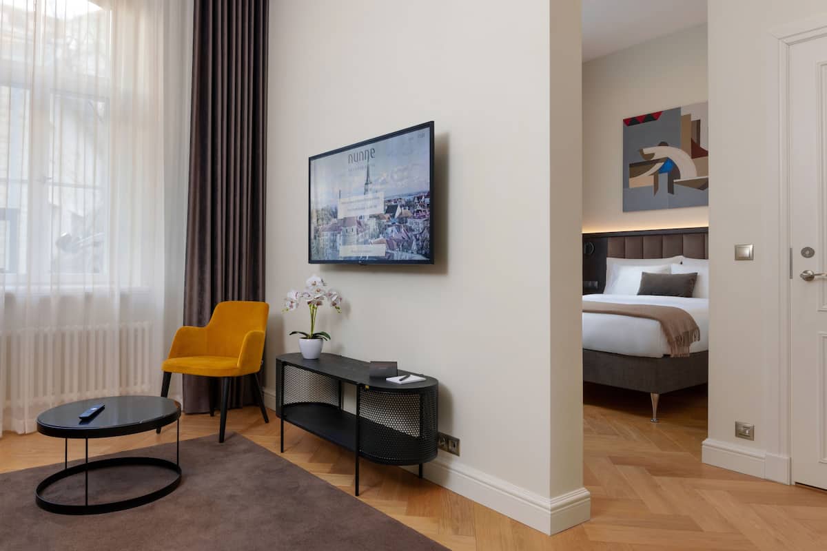 Ein modernes Hotelzimmer mit Bett, Nachttisch, Sessel und einem großen Fenster mit Vorhängen.