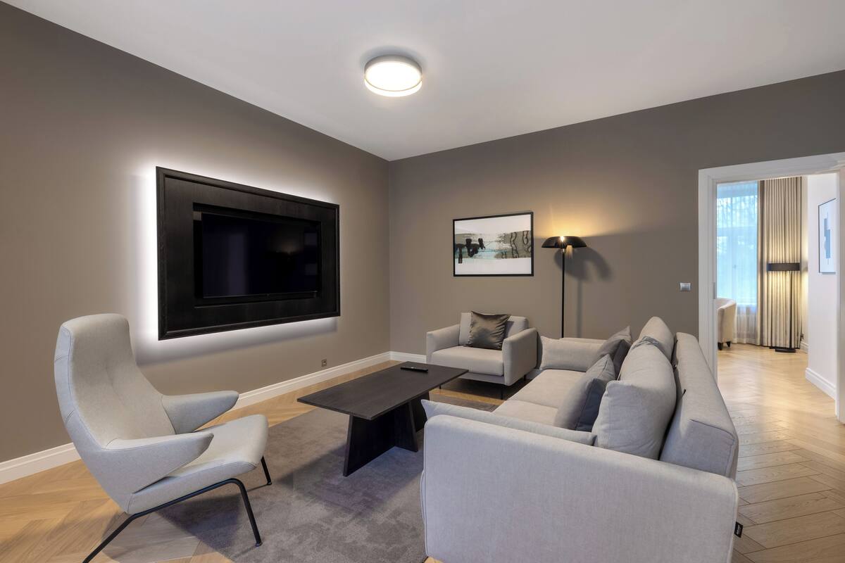 Ein modernes Wohnzimmer mit einem an der Wand befestigten Flachbildfernseher, einer Sofagarnitur, einem Couchtisch und einer Stehlampe.